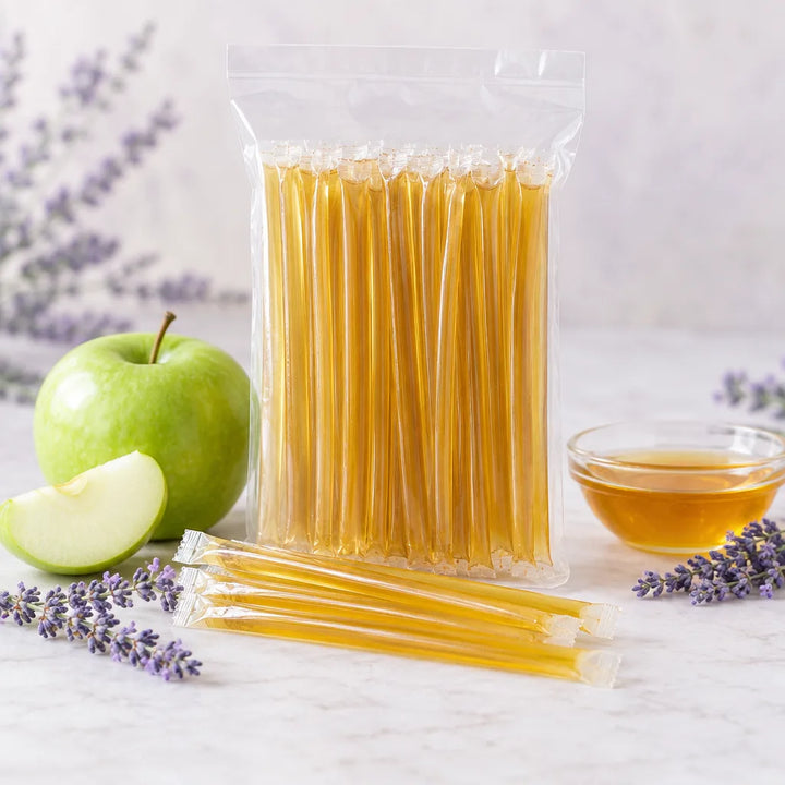 Lavender Green Apple Honey Sticks in a clear bag beside a green apple, a honey dish and lavender