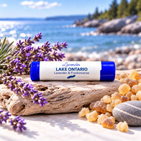 Lavender Lake Ontario Lip Balm in a blue tube on driftwood with lavender and resin pieces by water.
