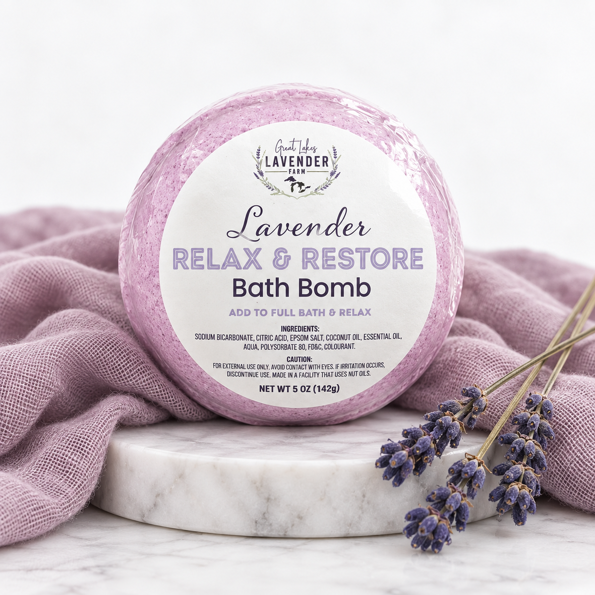 Lavender Relax & Restore Bath Bomb 5 oz in label wrap on a marble round with purple cloth and lavender