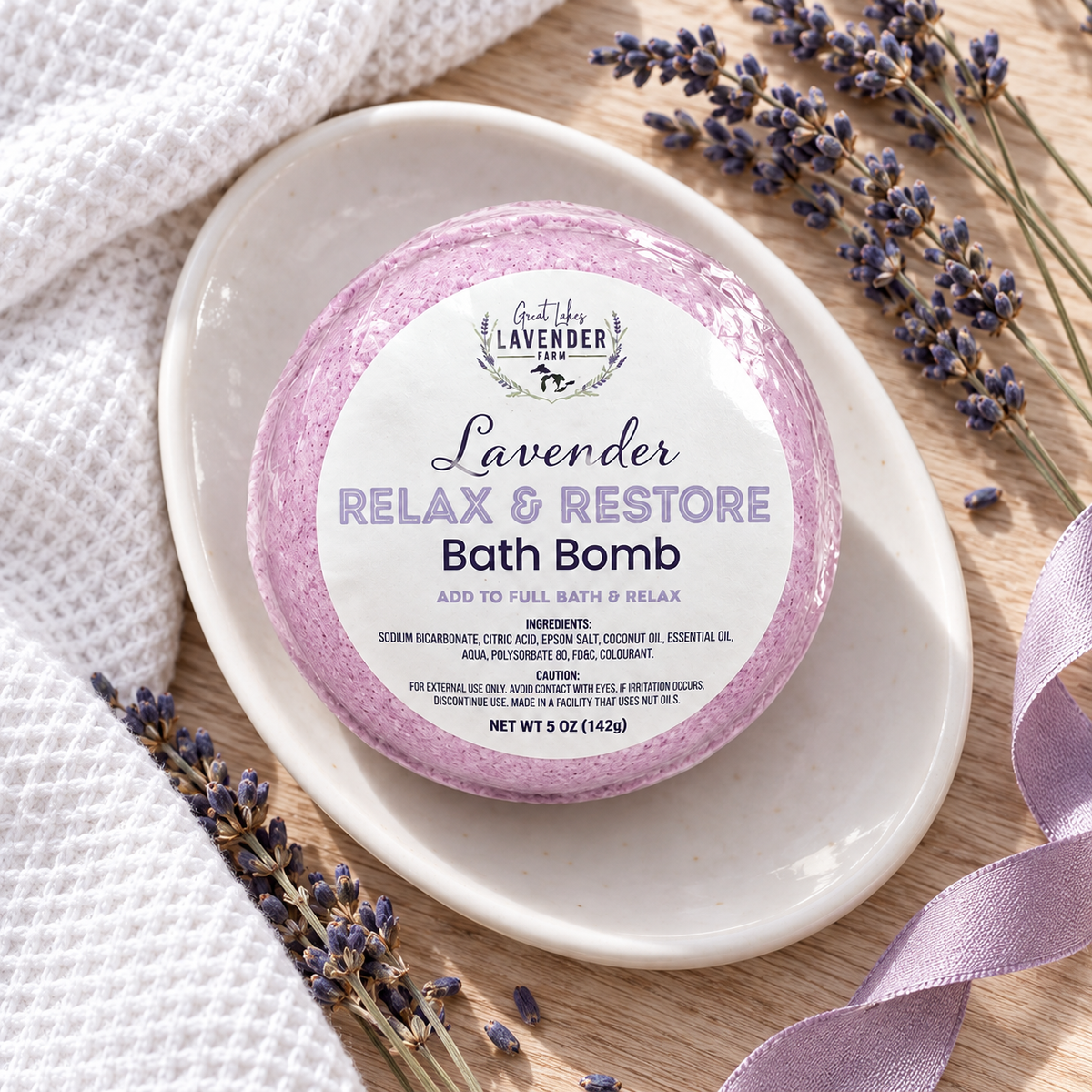 Lavender Relax & Restore Bath Bomb in label wrap on a white dish with lavender and ribbon