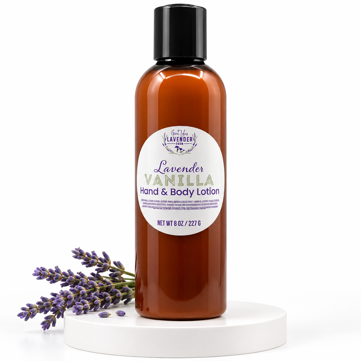 Lavender Vanilla Hand & Body Lotion amber bottle on a white round stand with a lavender sprig