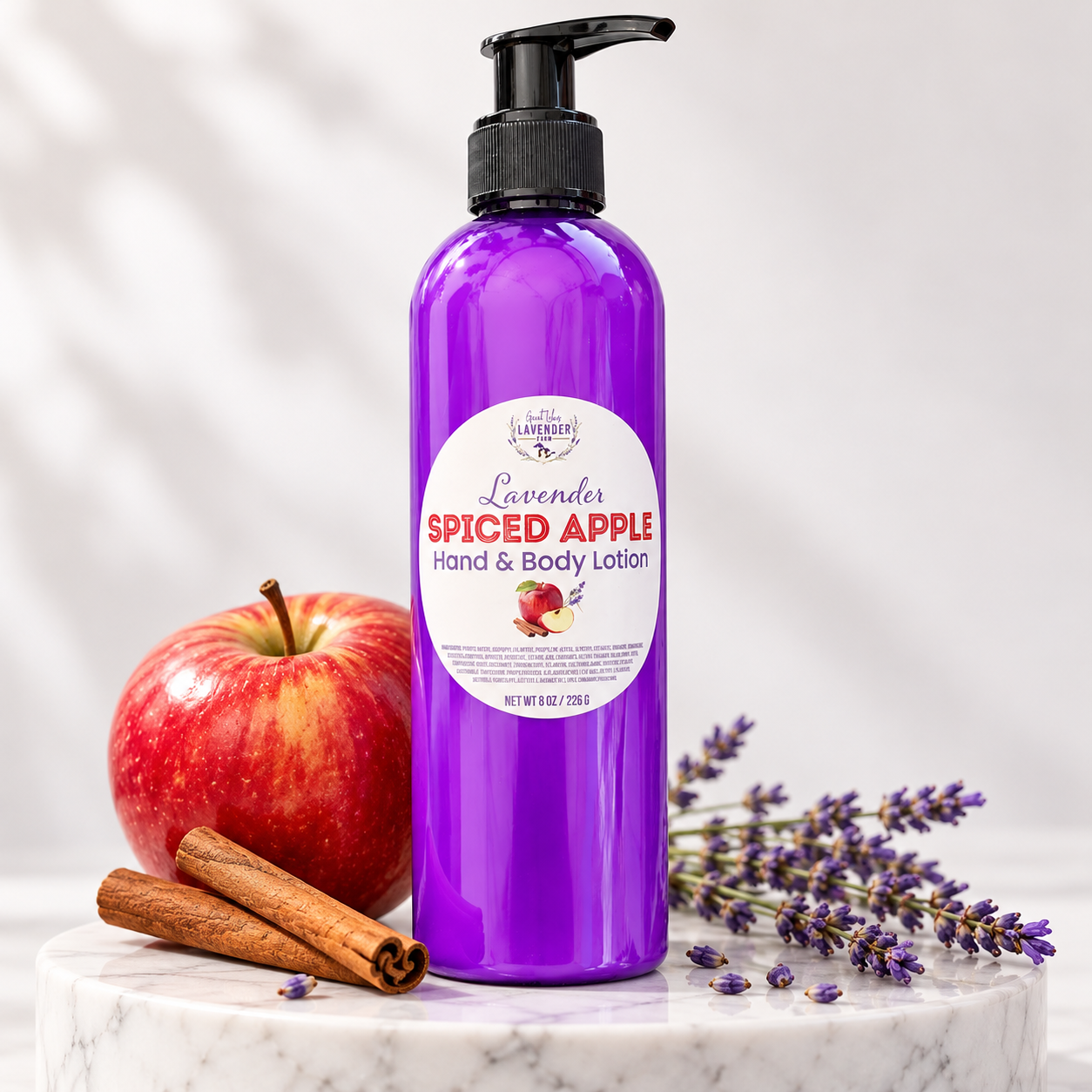 Lavender Spiced Apple Hand & Body Lotion in a purple pump bottle with a red apple, cinnamon sticks and lavender