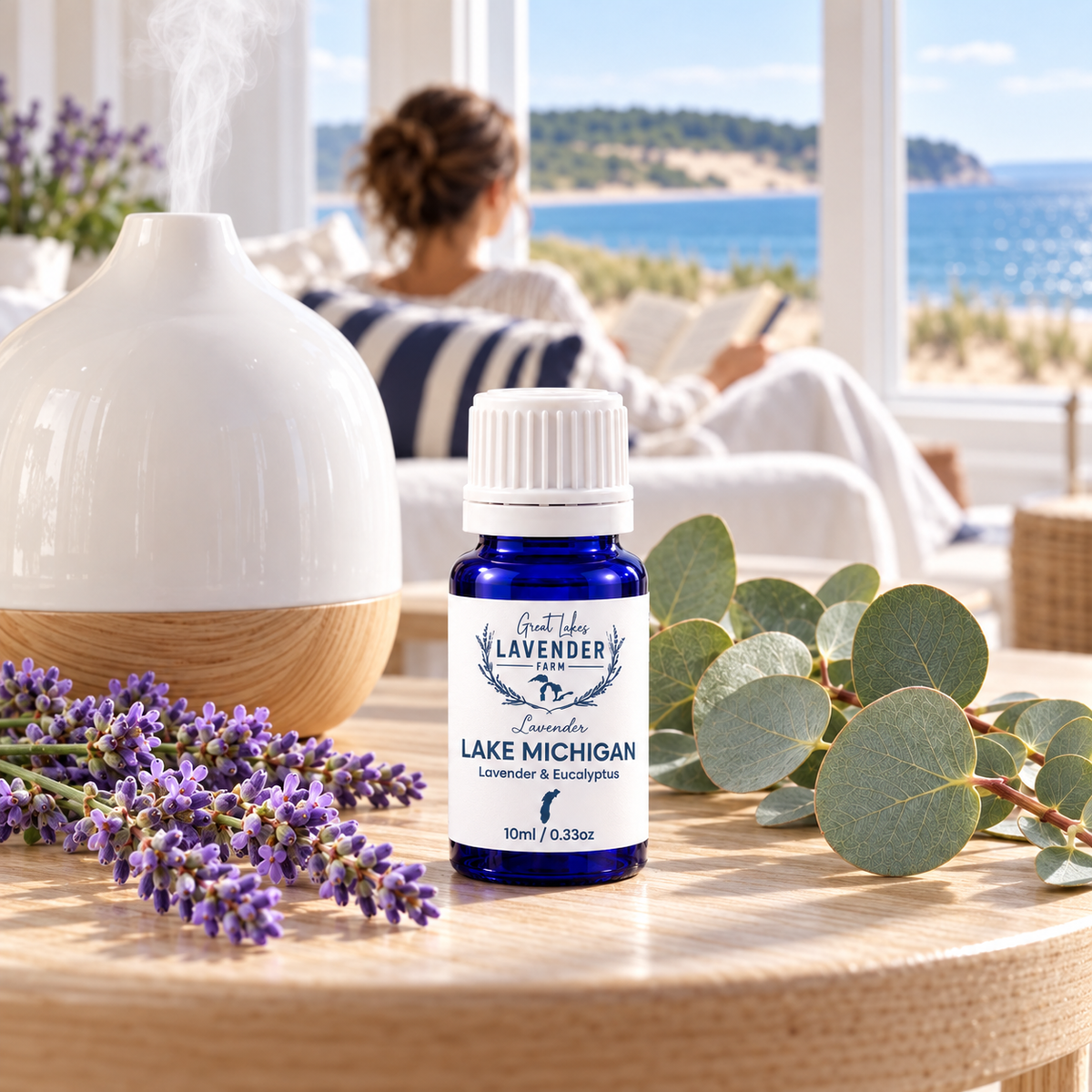 Lavender Lake Michigan Essential Oil bottle beside a diffuser, woman reading by a lake view window