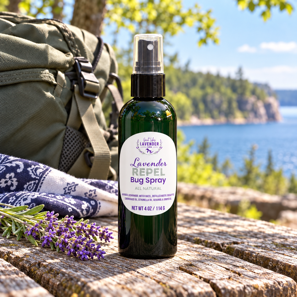Lavender Repel Bug Spray on a weathered table beside a backpack and blanket with a lake and cliffs behind