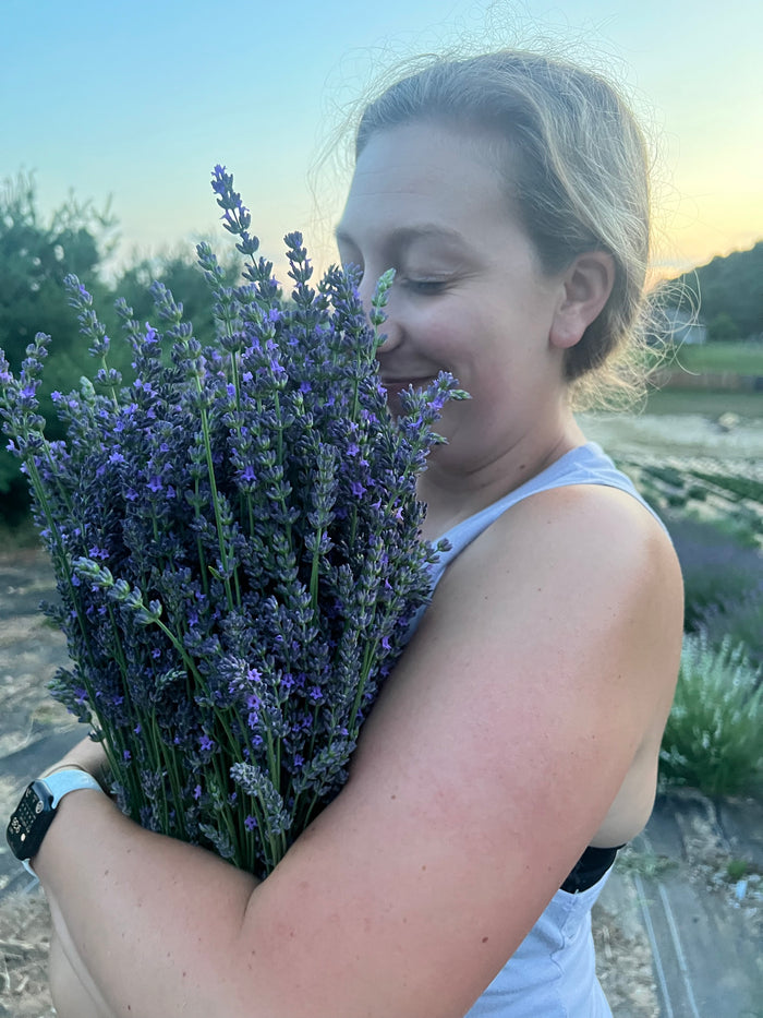 Woman smiling with eyes closed, breathing in a bundle of fresh lavender