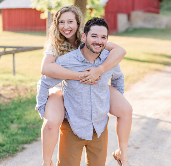 Sierra and Andrew smiling, Sierra riding piggyback, red barns behind them