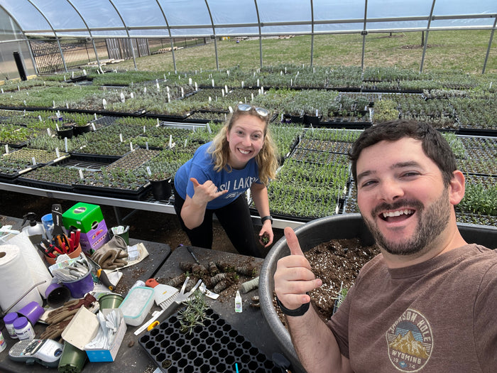 Two people giving shaka signs at a greenhouse potting bench
