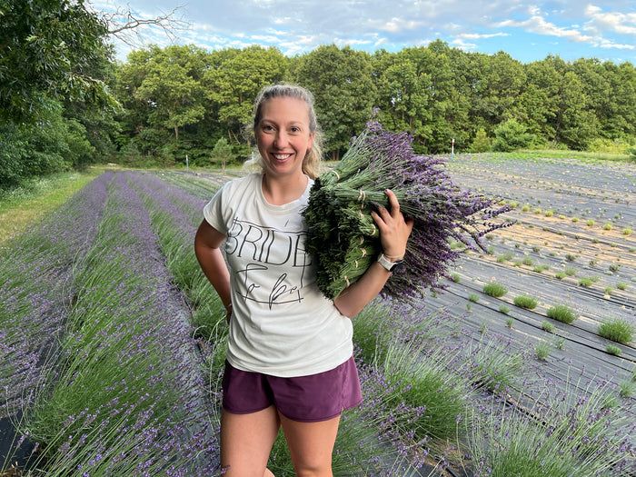 Woman in a bride to be shirt holding lavender bundles in the rows