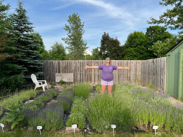 Woman with arms spread wide in a backyard garden of labeled lavender plants