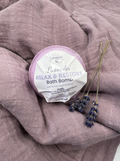 Lavender Relax & Restore Bath Bomb in shrink wrap on a draped mauve cloth with lavender sprigs