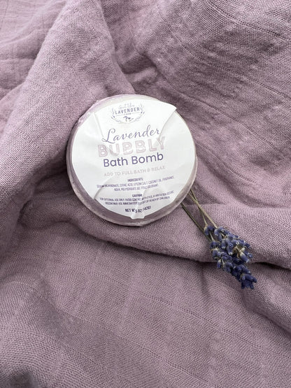 Lavender Bubbly Bath Bomb in shrink wrap on a draped mauve cloth with a lavender sprig